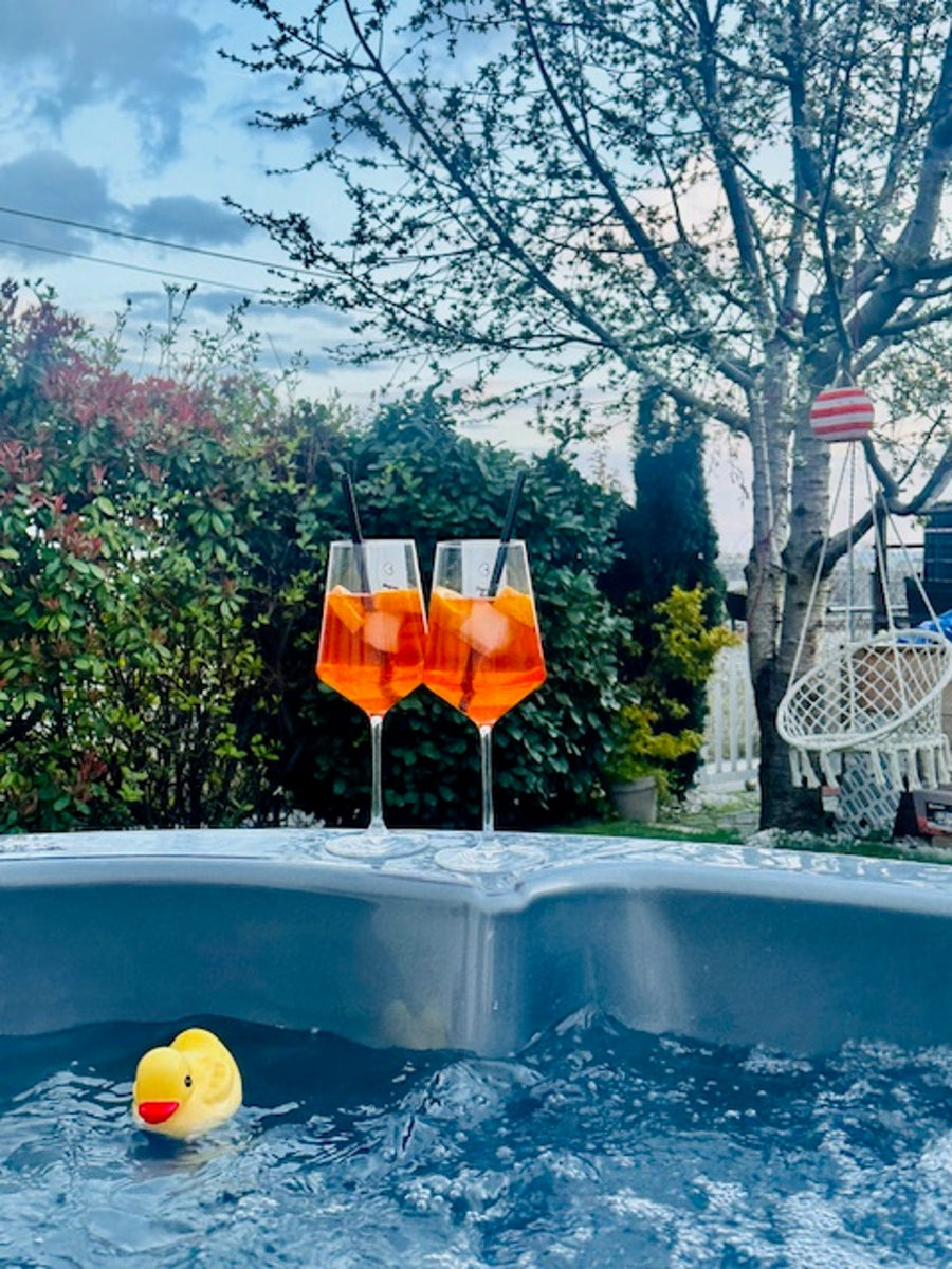 Hot Tub mit sprudelndem Wasser, Quietscheente und zwei Aperitifgläsern im Garten.