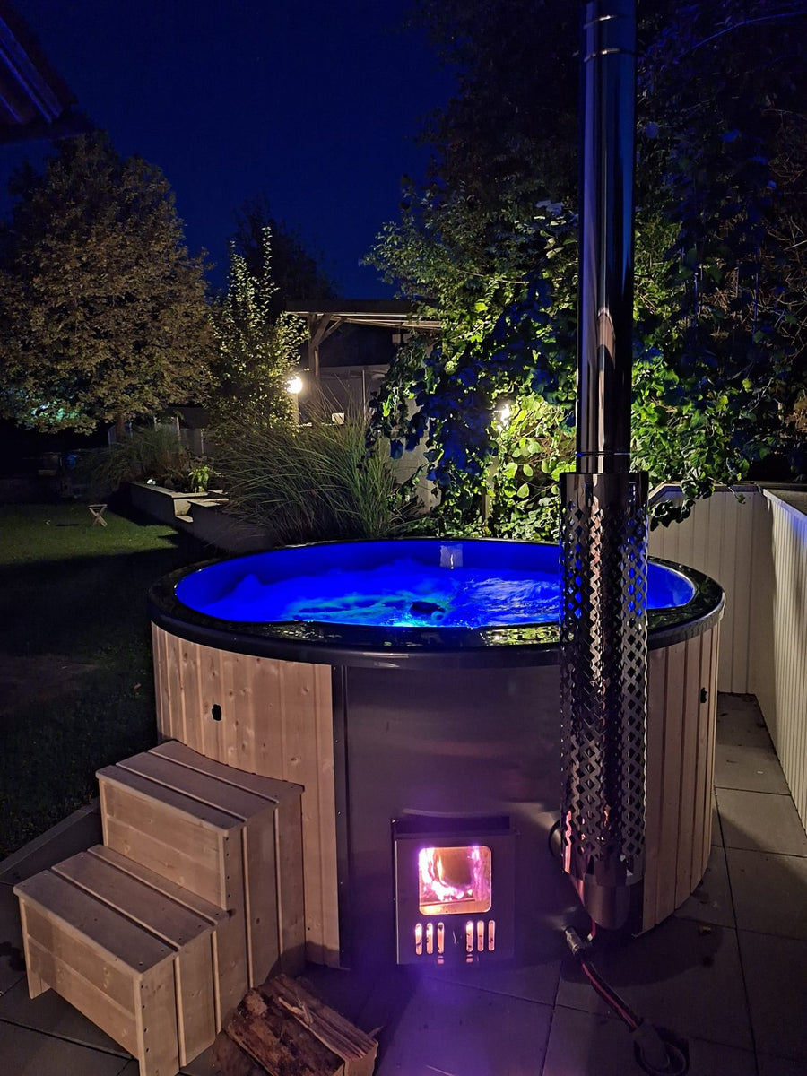 Hot Tub mit blau beleuchtetem Wasser und brennendem Holzofen bei Nacht.